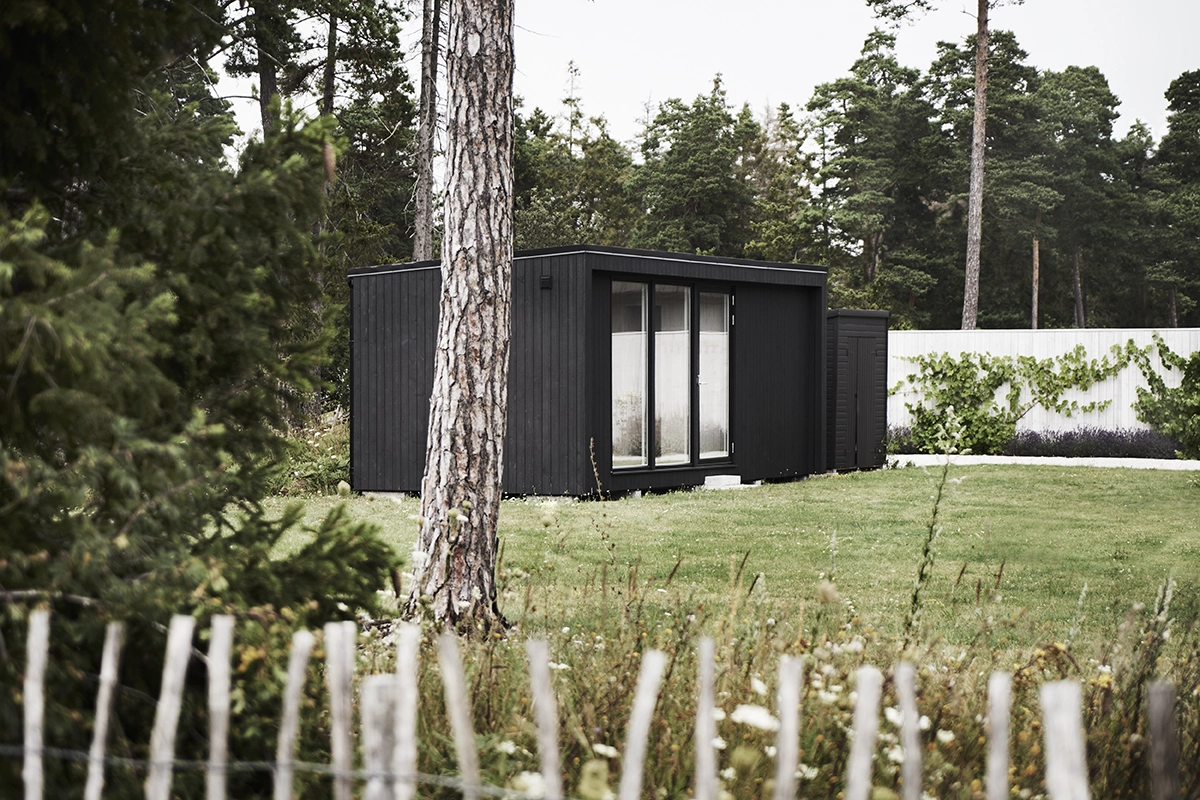 Attefallshus 25 kvm på en tomt. Huset är svart och har tre stora fönsterpartier