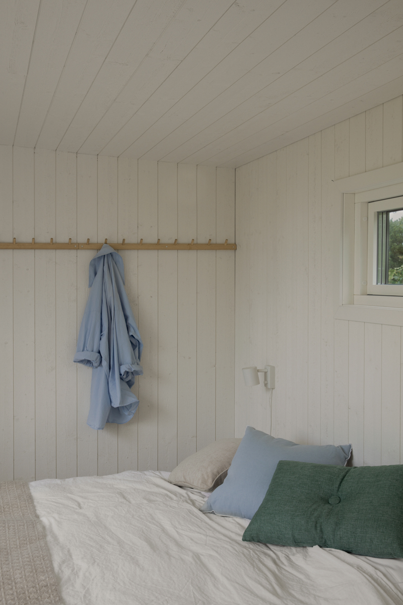 Insida av friggebod 10 kvm med väggar i vitmålad träpanel, inredd med säng och knopplist